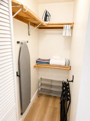 A compact closet with a hanging iron, a shelf with folded towels, and a metal rack for shoes. - Cozy studio with Kitchen + Free Parking + Central location in Miami. (Miami)