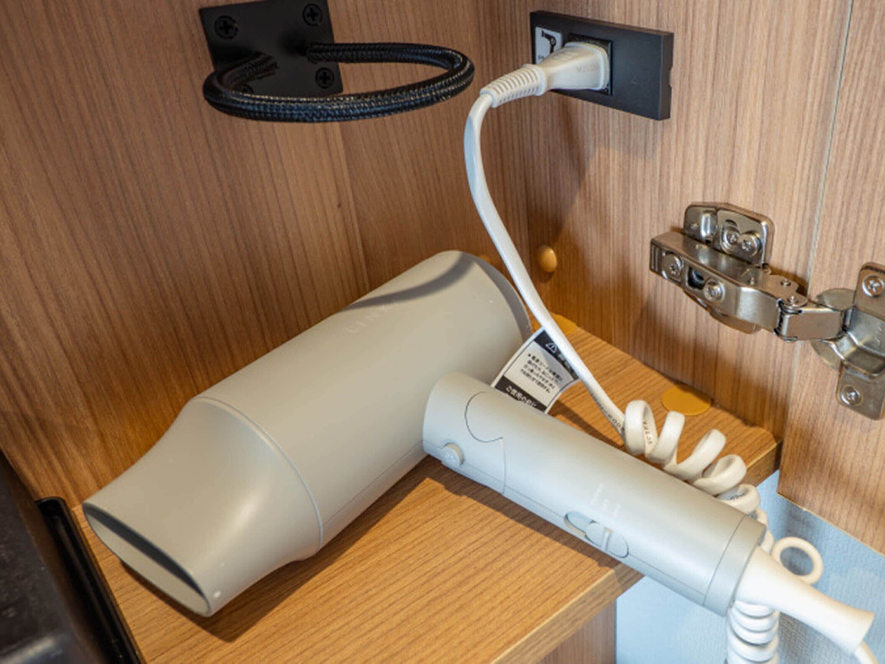 A hairdryer and phone charger on a wooden surface, connected to a wall socket.