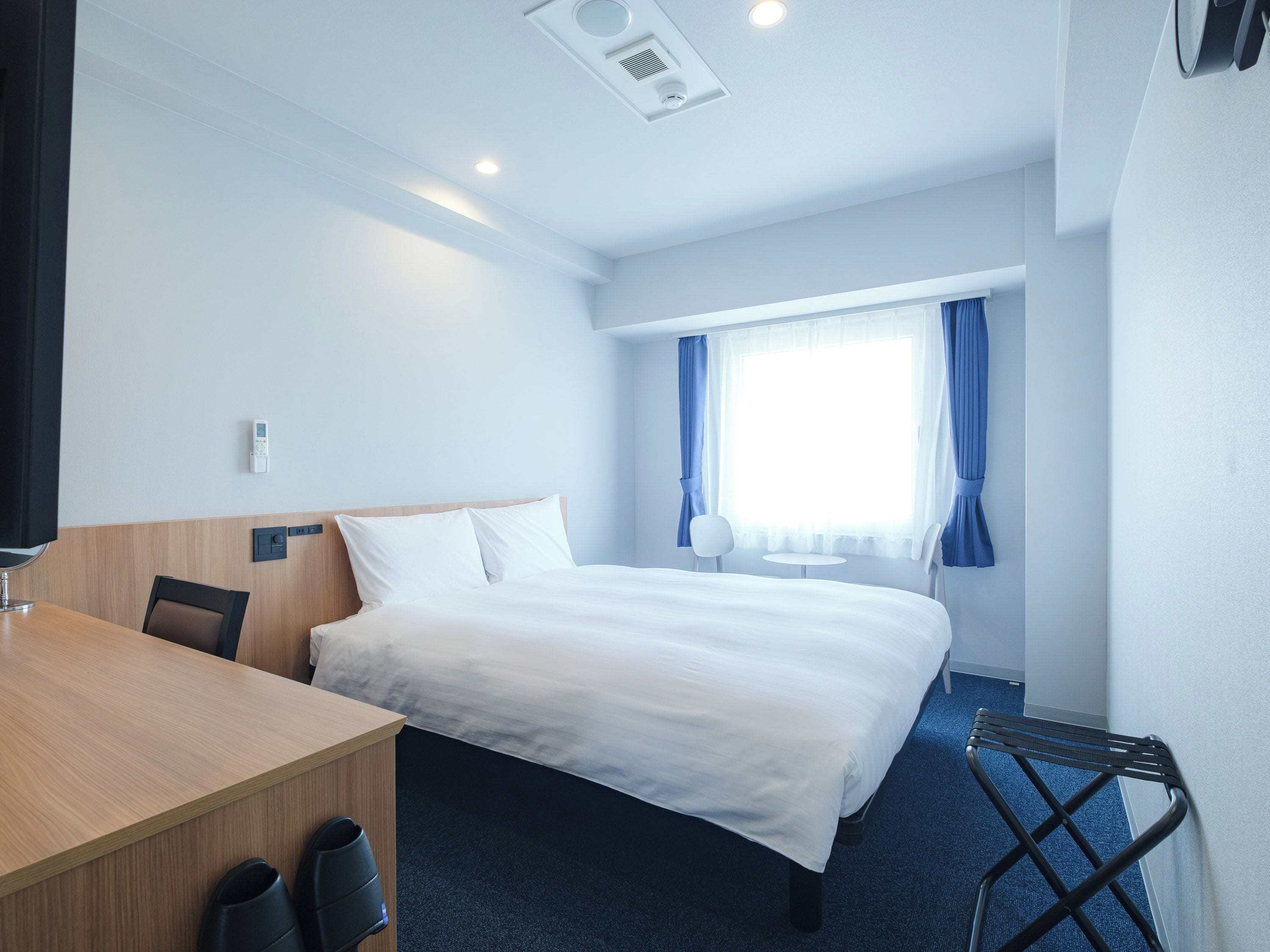 Una habitación de hotel con cama, escritorio, silla y una mesita.