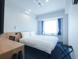 Una habitación de hotel con cama, escritorio, silla y una mesita.