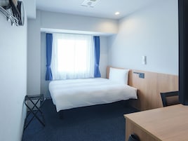 A hotel room with a bed, a desk, a chair, a window with curtains, and a ceiling light.
