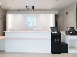 A reception desk with a neon sign, two nameplates, and a self-service kiosk.