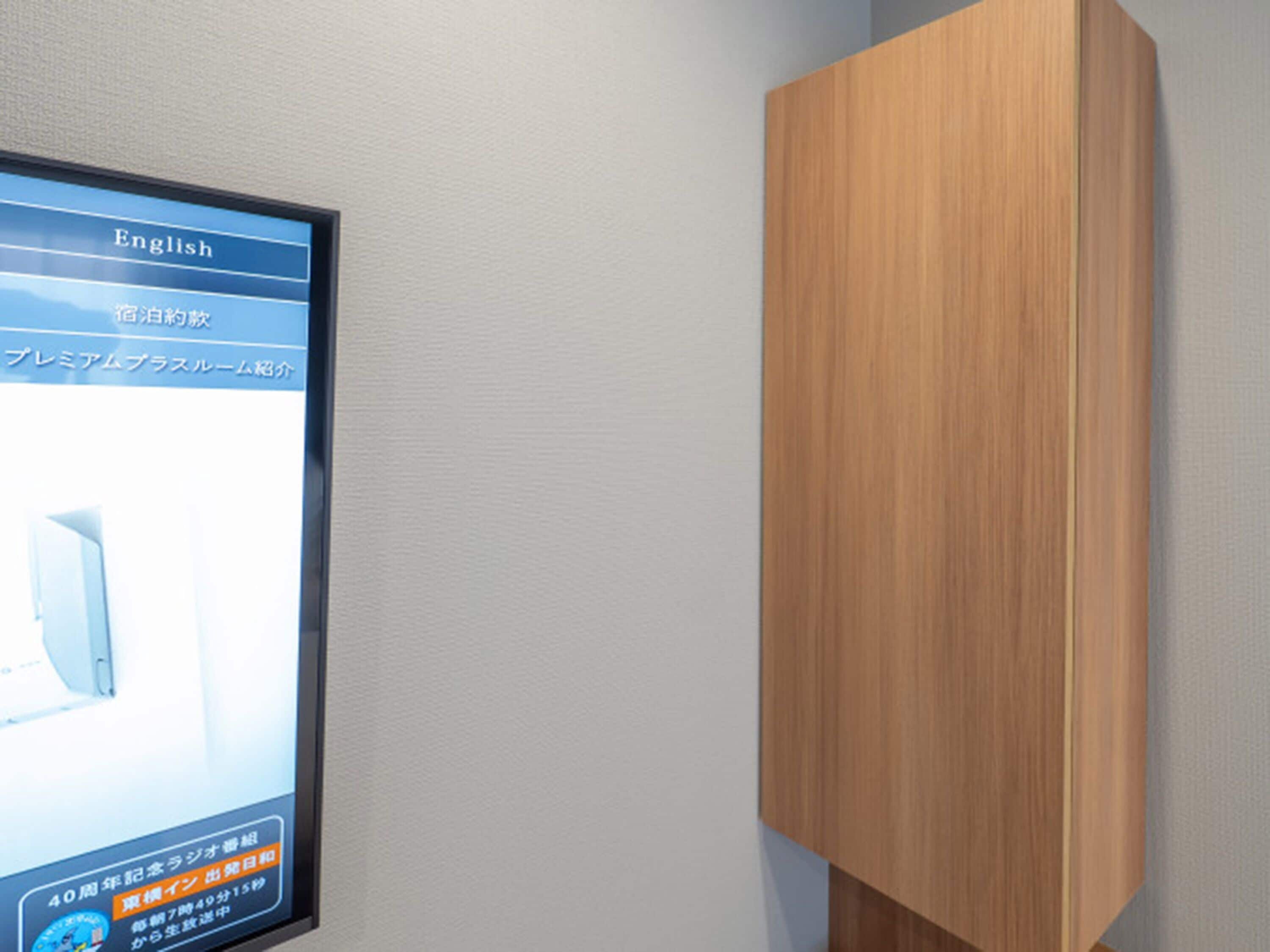 Una pantalla digital montada en la pared con texto en inglés y japonés, un mueble de madera y una pared con textura.
