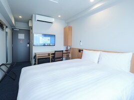 A hotel room with a bed, desk, chair, and an air conditioning unit.