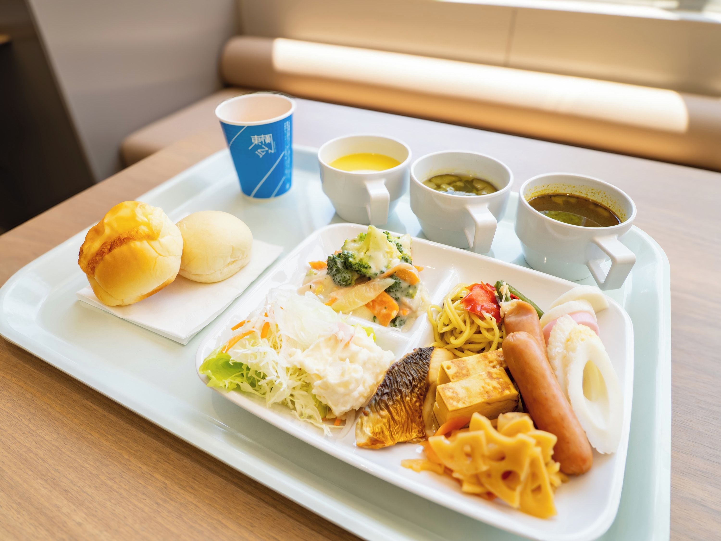 A safata amb una varietat d'aliments, com ara ensaïmades, fideus i un plat de peix, acompanyats de petits cuillers de sopa i salses.