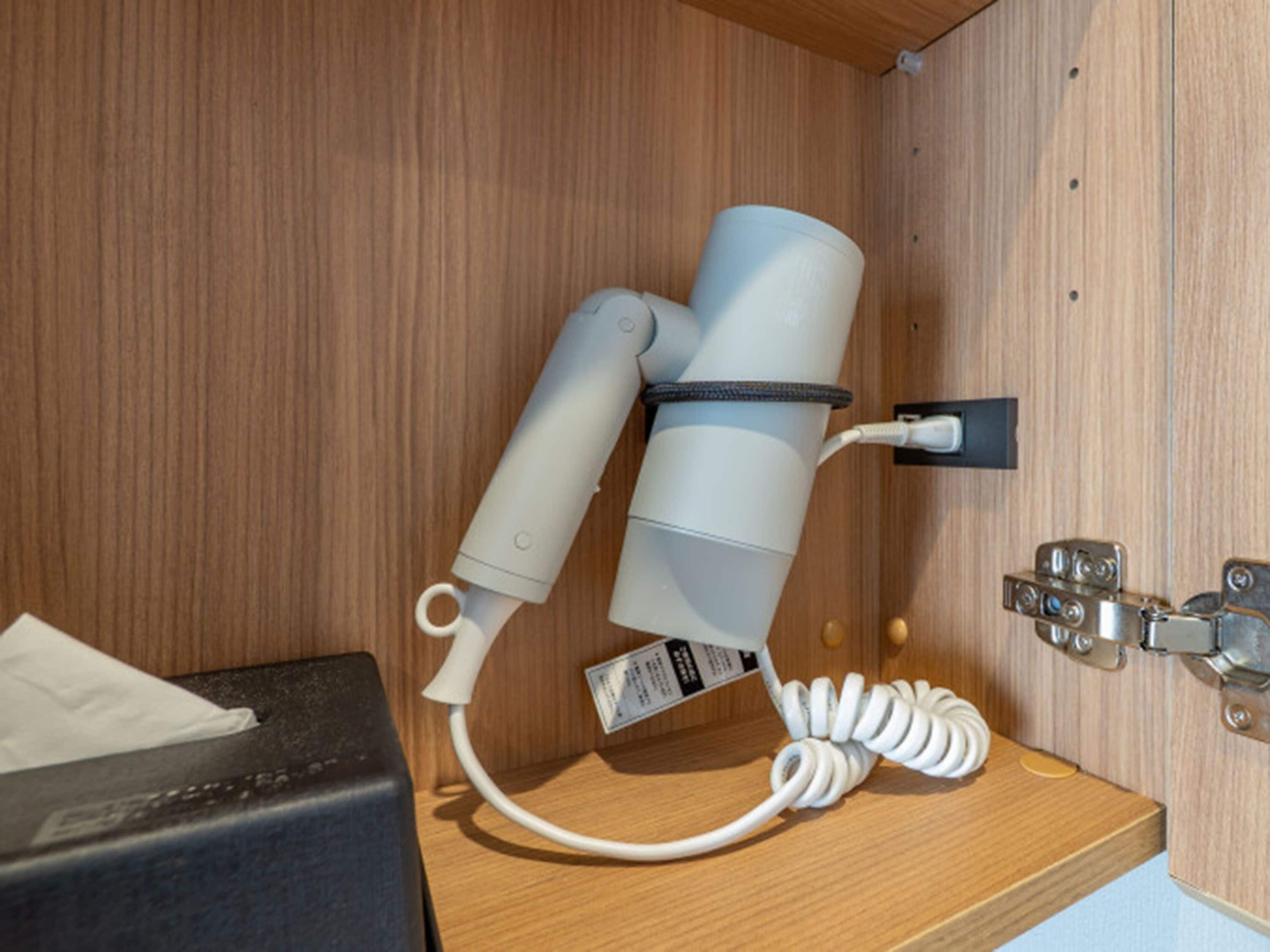 Un sèche-cheveux fixé au mur et une prise électrique sur une étagère en bois.