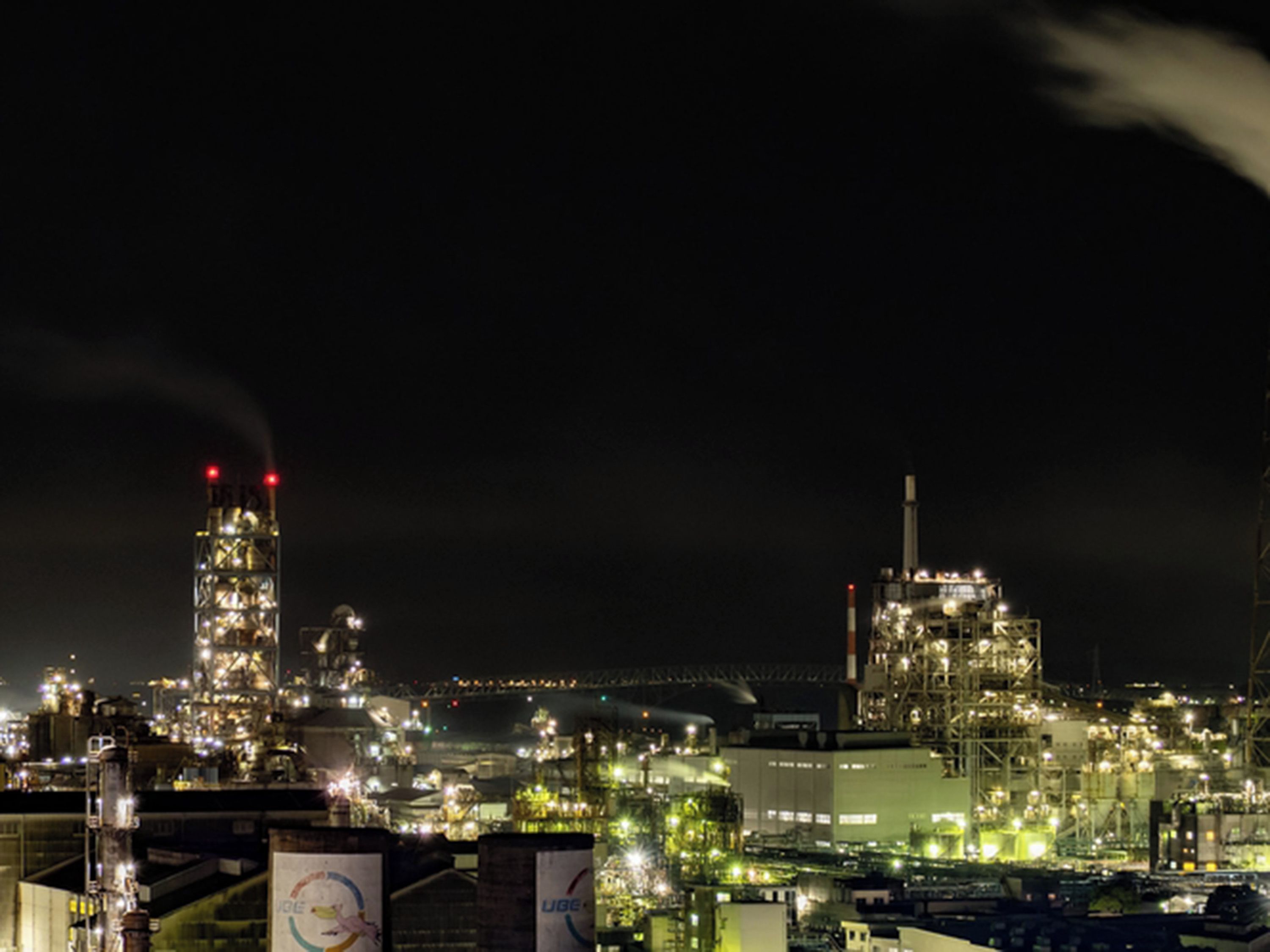 An industrial facility at night with illuminated structures and smokestacks.