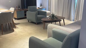 Una sala moderna con sofá, sillón, mesa de centro, televisor y un comedor con sillas y una mesa.