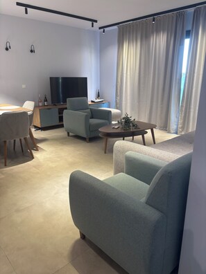 A modern living room with a sofa, armchair, coffee table, TV, and a dining area with chairs and a table. - Beach apartment Wünderschon (Vourvouro)