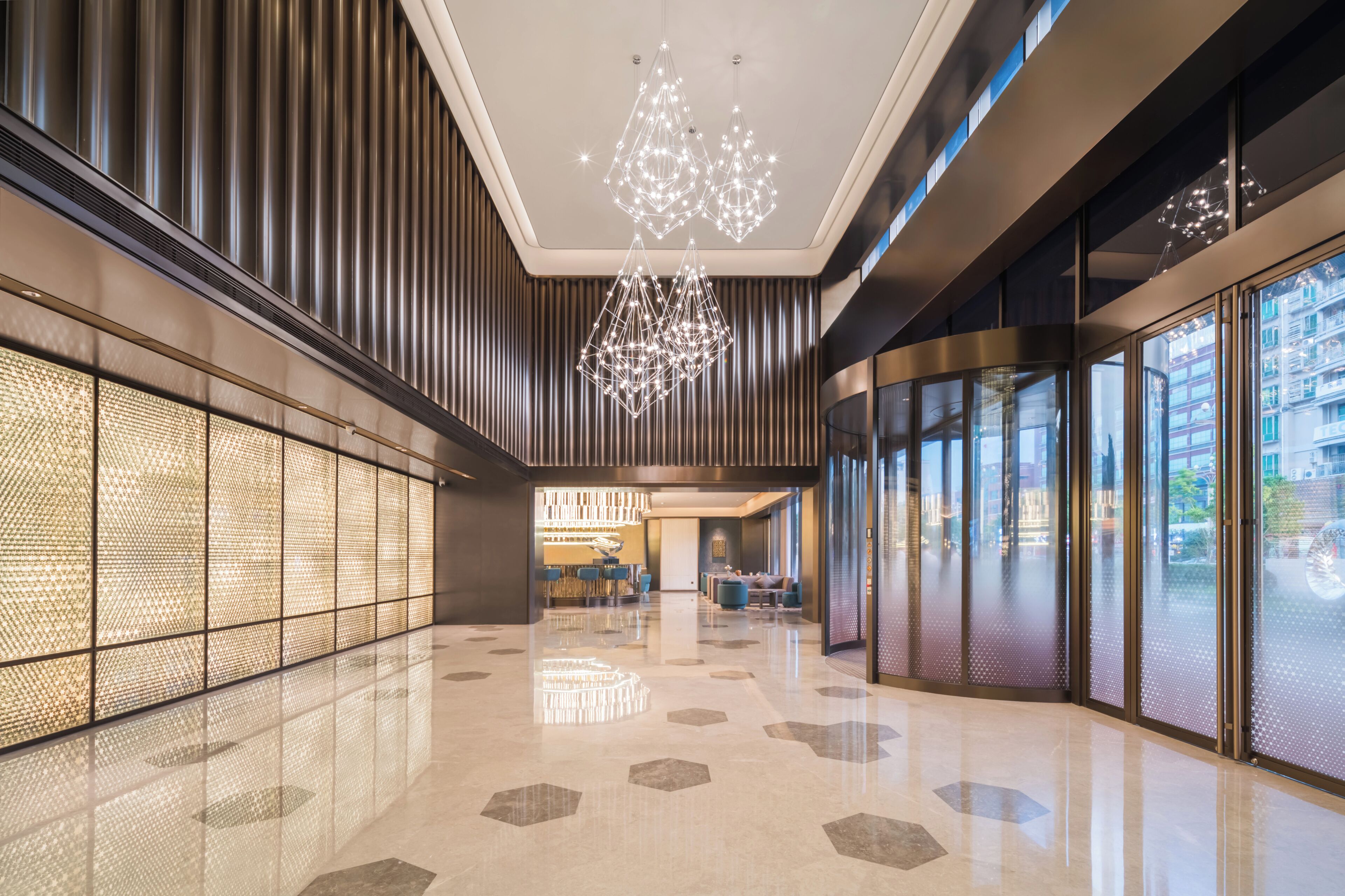 Un moderno vestíbulo de hotel con piso reflectante, paredes de diseño geométrico e iluminación contemporánea.