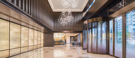 Un moderno vestíbulo de hotel con piso reflectante, paredes de diseño geométrico e iluminación contemporánea.