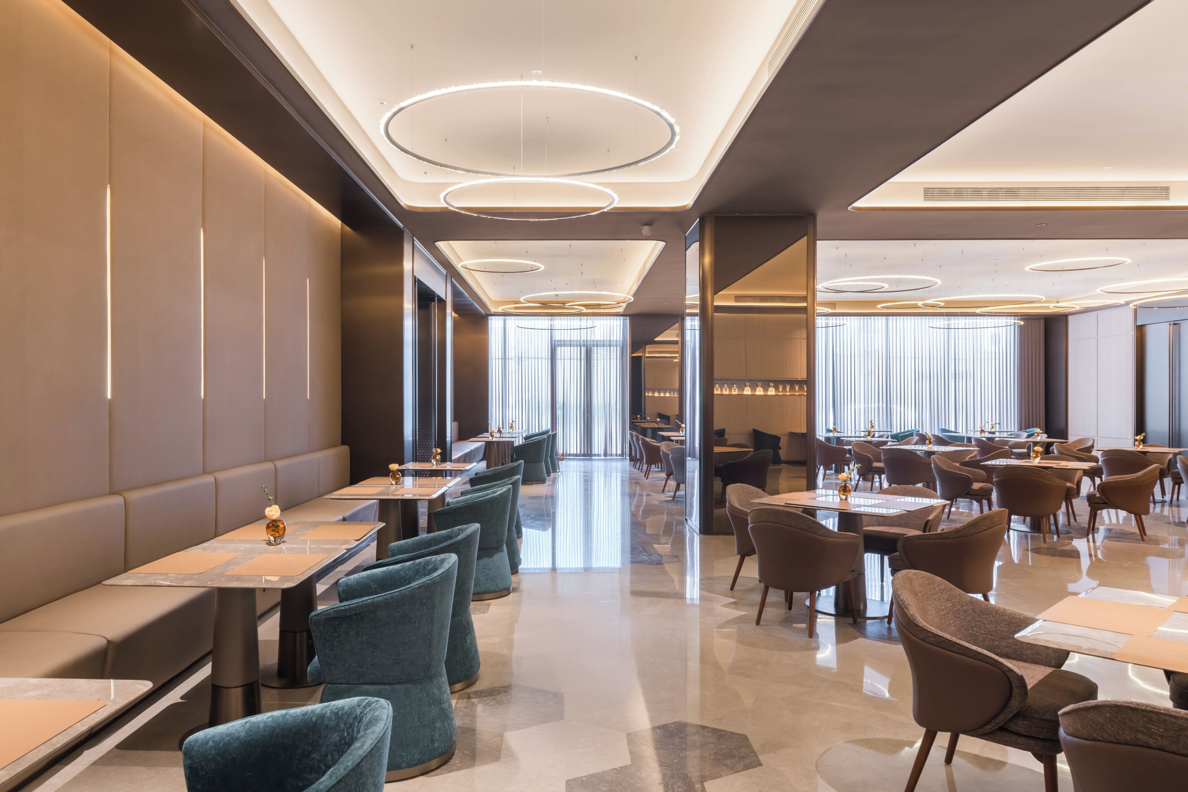 Een moderne hotellobby met een lange receptiebalie, meerdere zithoeken en een groot raam dat natuurlijk licht binnenlaat.