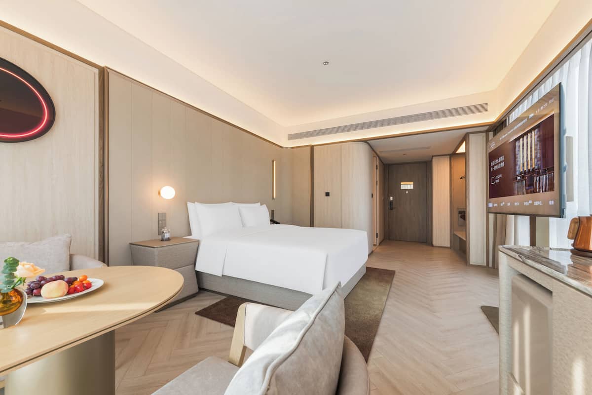 A modern hotel room with a bed, bedside table, and a small seating area.