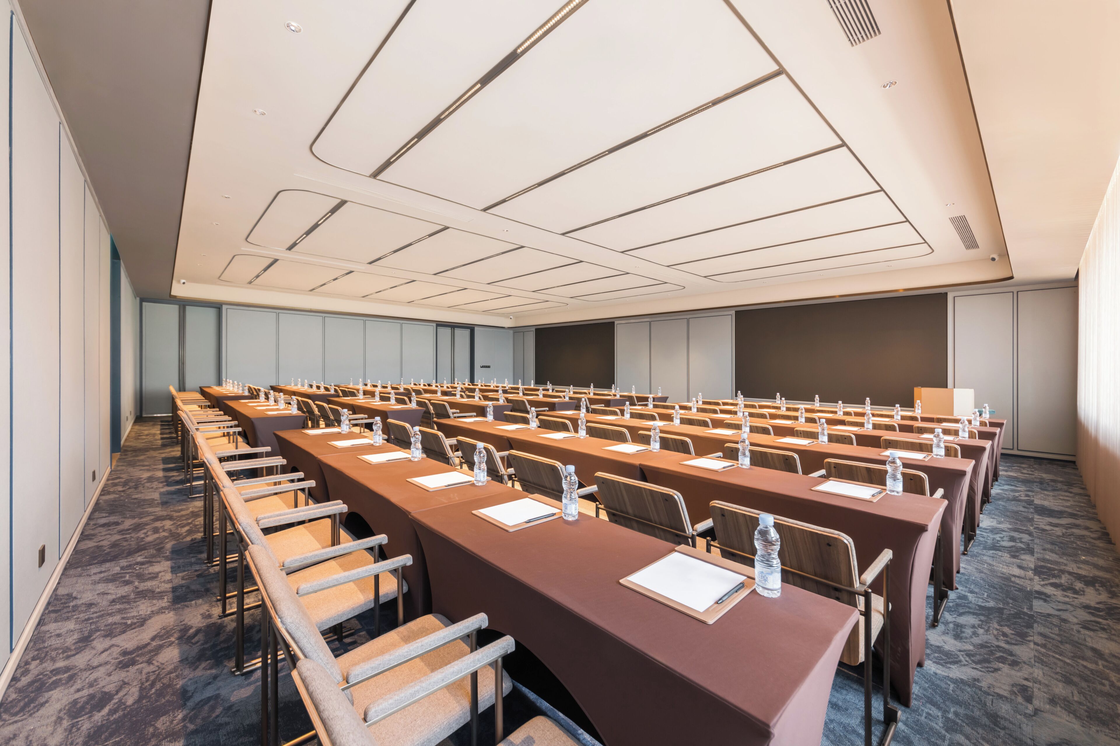 A conference room with rows of tables and chairs, a projector screen, and a carpeted floor.