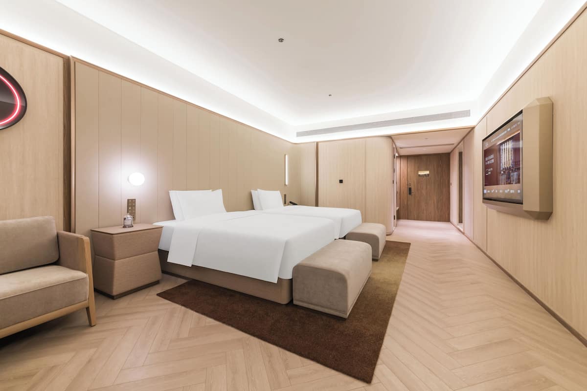 A modern hotel room with a large bed, a sofa, a nightstand, and a flat-screen TV.