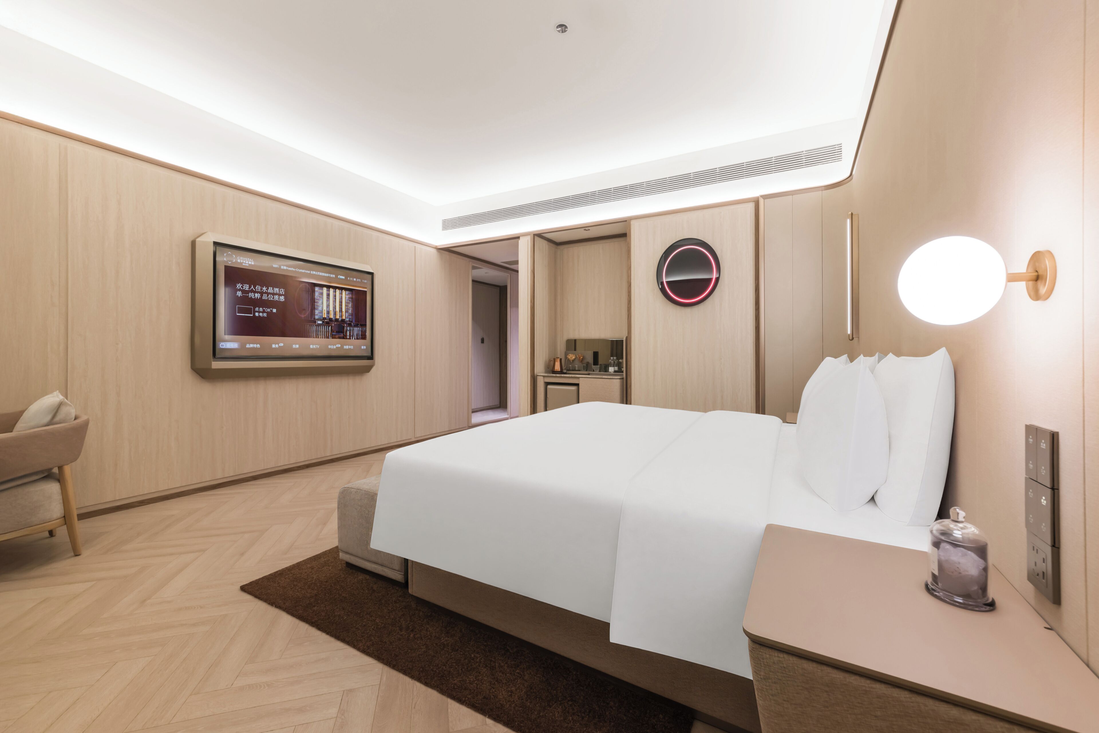 Una habitación de hotel moderna con una cama grande, televisión, mesita de noche con lámpara y un armario pequeño.