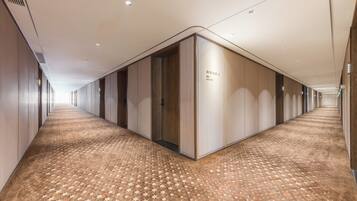 A long, narrow hotel corridor with a patterned carpet, wooden walls, and recessed lighting.