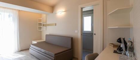 A modern room with a bed, a desk, and a chair. There is a door leading to another room.