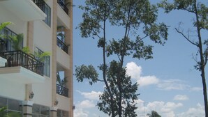 A swimming pool with lounge chairs, a tall tree, and a multi-story building with balconies. - STUNG SANGKE HOTEL (Battambang)