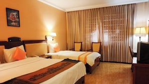 Una camera d'albergo con due letti, una scrivania, una sedia e un'ampia finestra con tende.