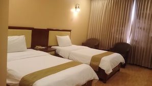 Una camera d'albergo con due letti, una scrivania, una sedia e una finestra con tende.