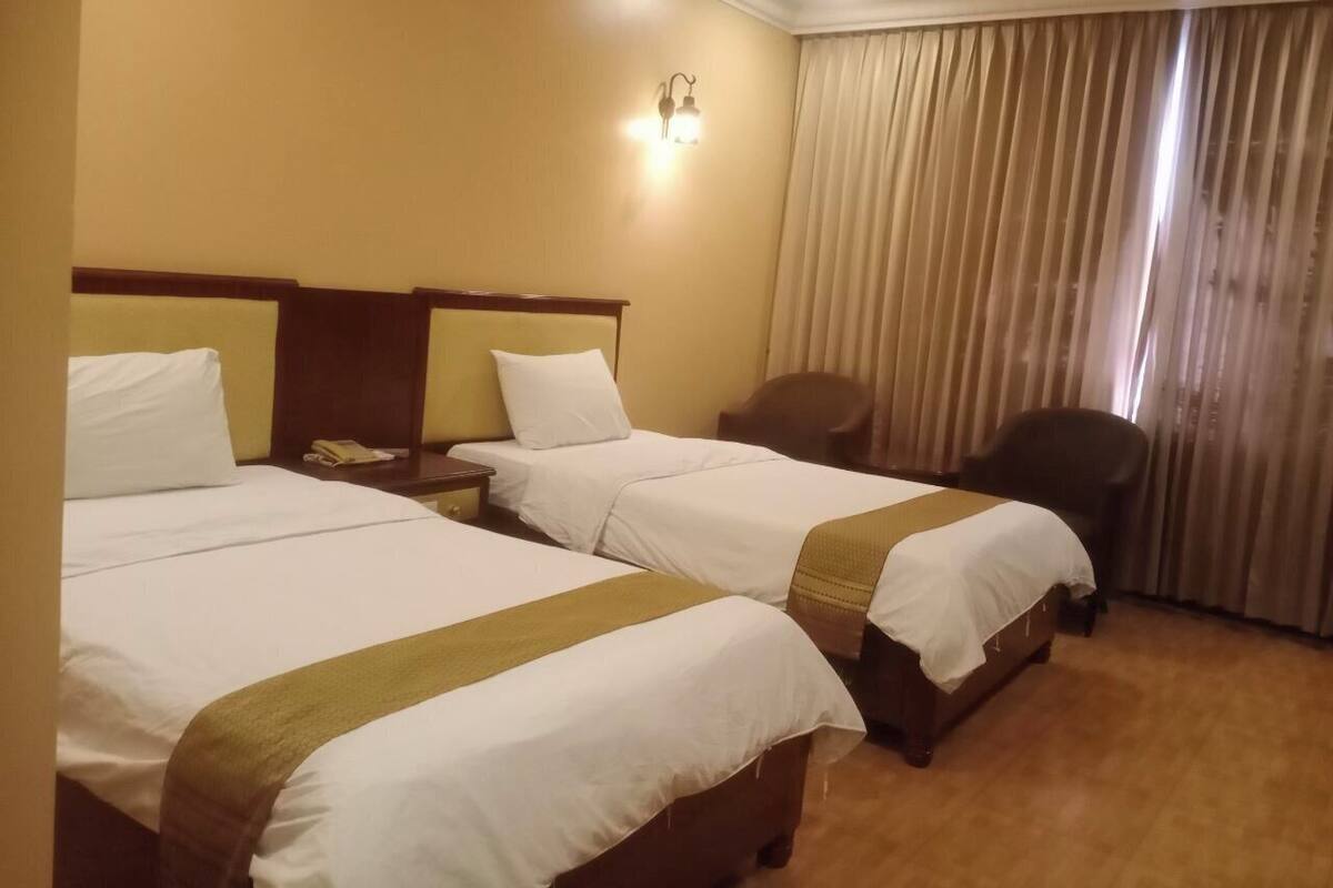 A hotel room with two beds, a desk, a chair, and a window with curtains.