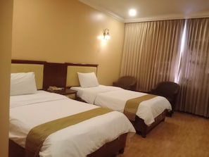 Una habitación de hotel con dos camas, un escritorio, una silla y un ventanal con cortinas.