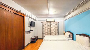 A hotel room with two beds, a TV, a wardrobe, and a small table. - Thepmongkol House (Bangkok)