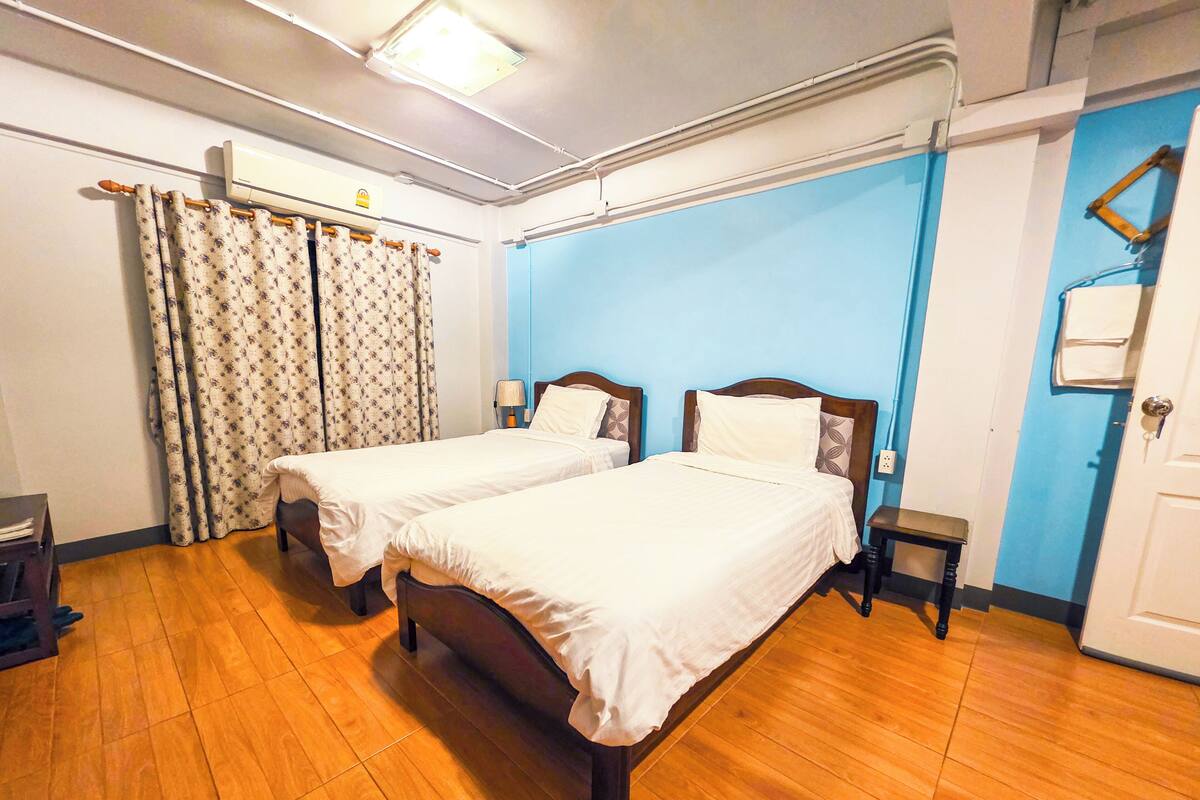 A hotel room with two beds, wooden flooring, a blue accent wall, and a ceiling light.