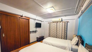 A hotel room with two beds, a TV, a wardrobe, and a curtain. - Thepmongkol House (Bangkok)