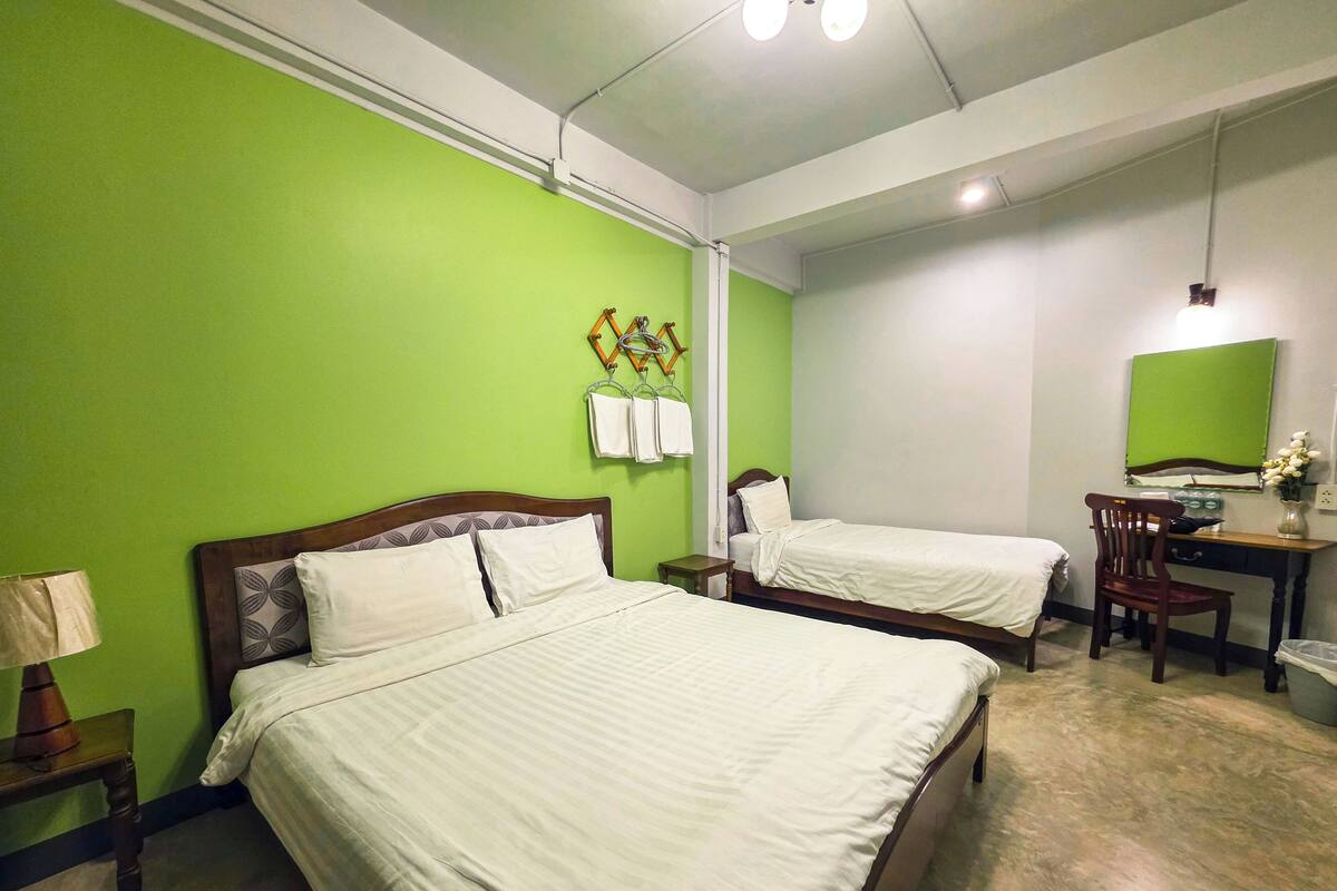 A hotel room with two beds, a desk, a chair, a lamp, and a green wall.