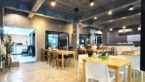 A spacious dining area with wooden tables and chairs, a kitchen area with modern appliances, and a view into the dining room. - Thepmongkol House (Bangkok)