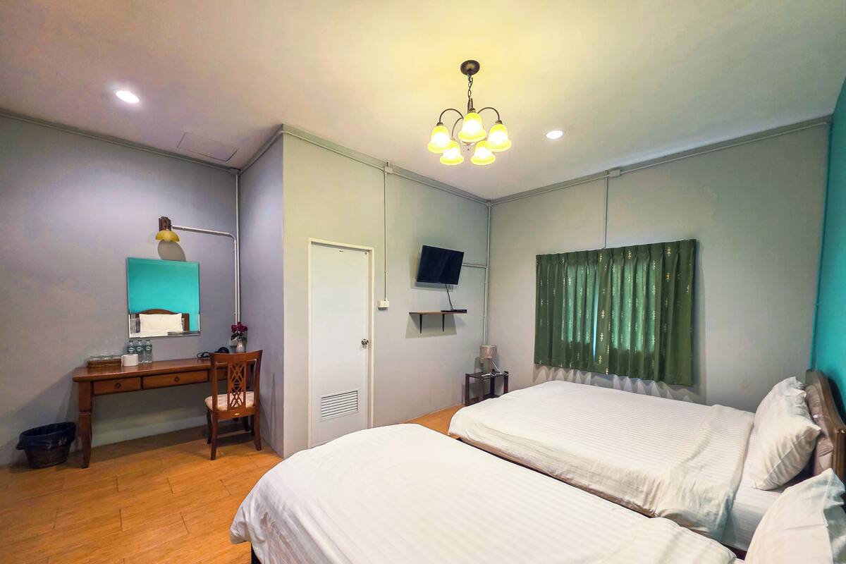 A bedroom with two beds, a desk with a chair, a television, and a ceiling light fixture.