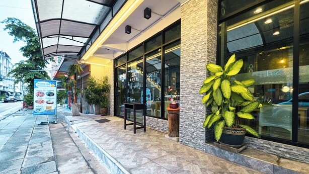 A restaurant with outdoor seating, a large potted plant, and a signboard. - Thepmongkol House (Bangkok)