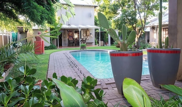 A swimming pool with surrounding greenery and a covered outdoor area.