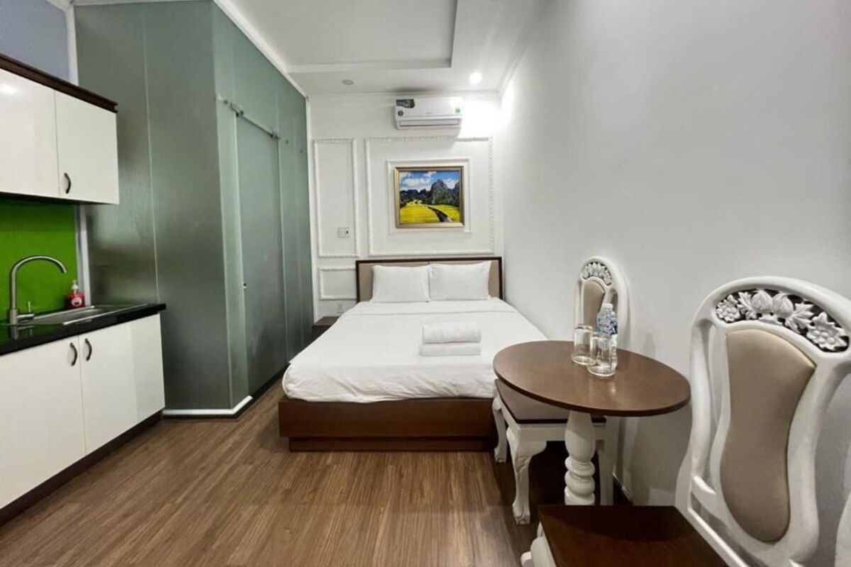 Ein kleines Hotelzimmer mit Bett, Esstisch, Stuhl, Küchenzeile und einem Bild an der Wand.