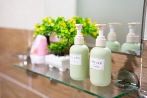 Ein Badezimmer mit einer Glasablage, auf der sich Flaschen mit Dâu Gôi Shampoo und eine pinke Flasche Duschgel befinden.