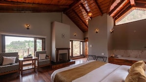 Un dormitorio con una cama grande, una chimenea, un conjunto de sofás y vistas al exterior.