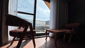 A room with a large window, a wooden table, and two patterned chairs. - EMROZ BY KINGS RESORT (Pahalgam)
