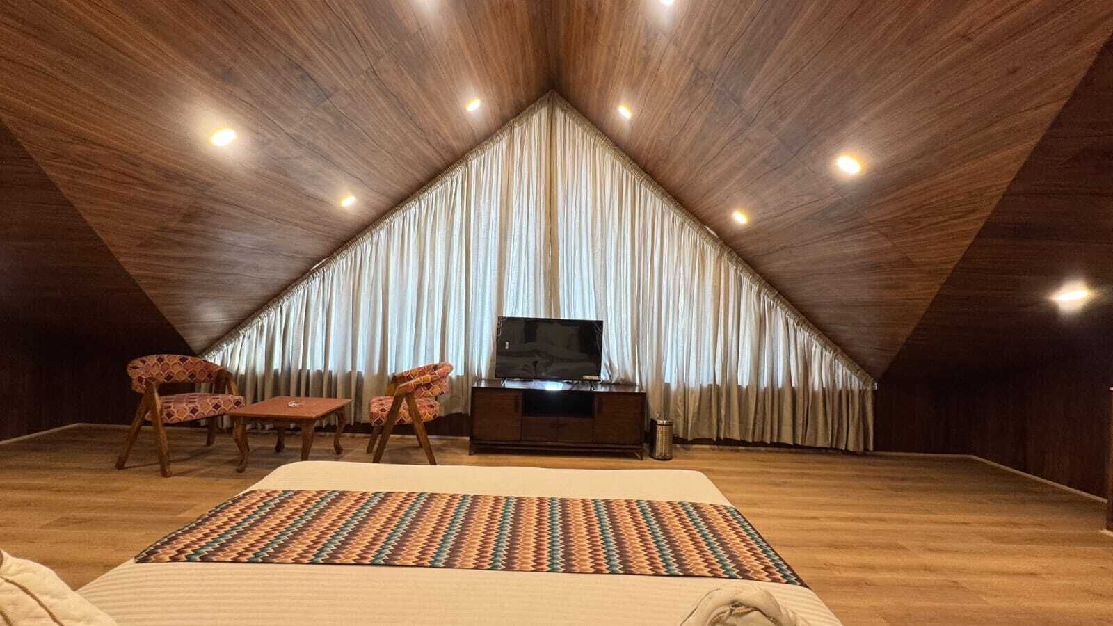 Habitación estilo ático con techos altos, una cama grande, un televisor y dos sillas.