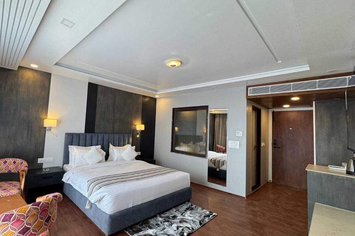 A modern hotel room with a large bed, bedside tables, a chair, a mirror, and a wardrobe.