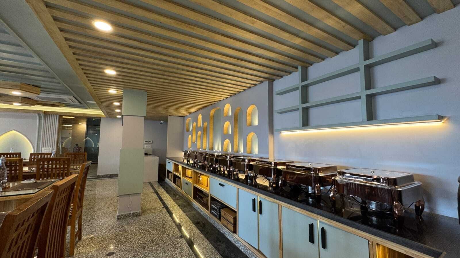 Uma área de buffet com um balcão extenso, várias máquinas de café e um espaço de estar com mesas e cadeiras.