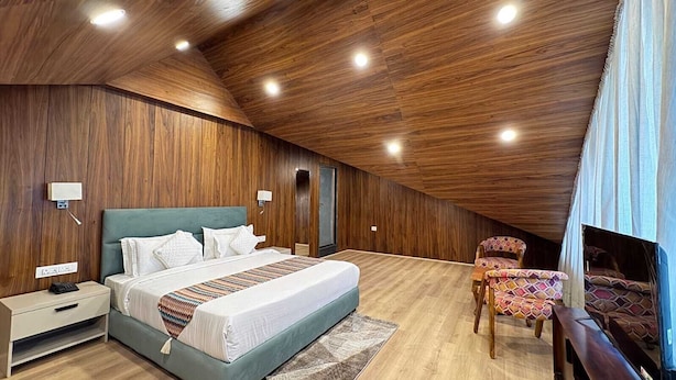 A bedroom with a wooden ceiling, a bed, bedside tables, a chair, and a window. - EMROZ BY KINGS RESORT (Pahalgam)