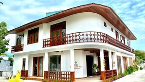 Un edificio de dos pisos con fachada blanca, balcones de madera y un letrero que dice 'ANA INN MALDIVES'.