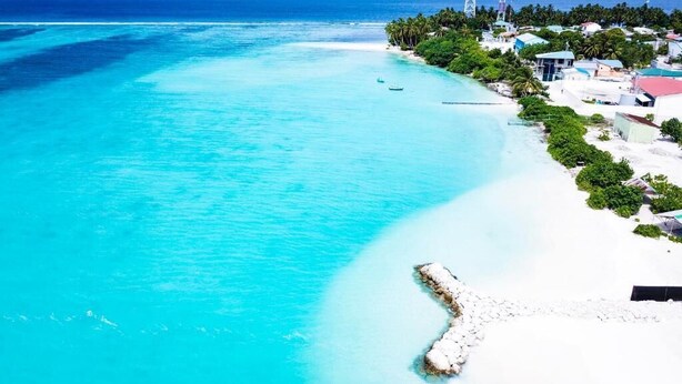 Una zona costera con aguas turquesas cristalinas, una playa de arena blanca y un pequeño muelle que se adentra en el mar.