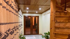 Una escalera de madera que conduce a una habitación con un cartel que dice 'Wall of Thanks', una puerta de madera y dos plantas en macetas.
