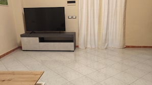 A living room with a flat-screen TV on a stand, a wooden table, and a curtain. - Cibali rooms (Catania)