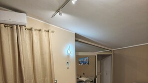 Een slaapkamer met een bed, een nachtkastje, een wandlamp en een deur naar een andere kamer.