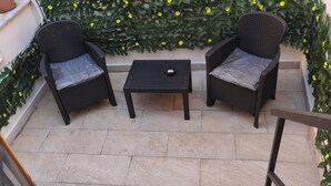 A patio with two wicker chairs, a small table, and a decorative wall with green foliage and yellow flowers. - Cibali rooms (Catania)