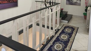 A staircase with a white railing, a blue patterned rug, and a painting of flowers on the wall. - Cibali rooms (Catania)